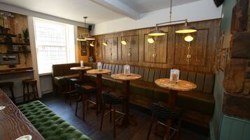 A cozy bar area with wooden paneling, leather seating, and pendant lighting.