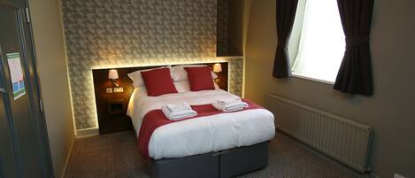 A neatly made bed with white and red bedding, a bedside lamp, and a window with curtains.