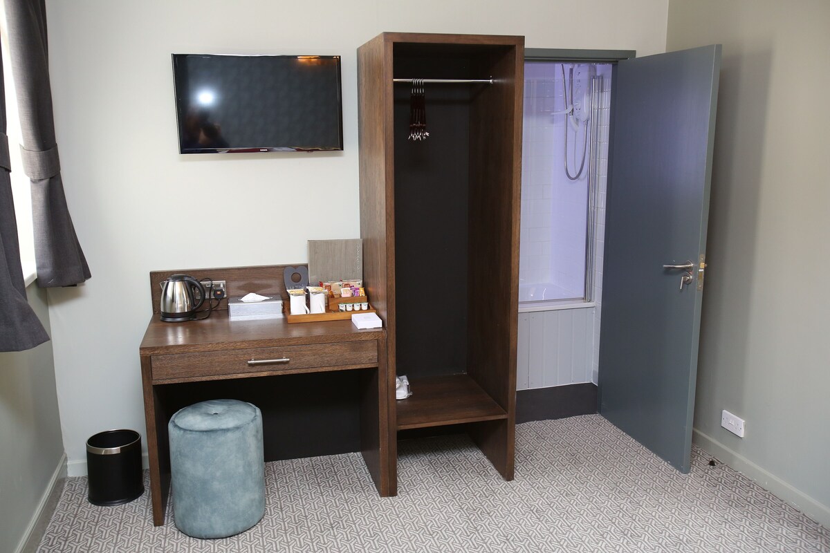 A room with a wooden desk, a television mounted on the wall, a shower area, and a door.