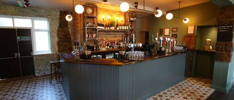 A bar area with a counter, shelves of bottles, and a variety of glasses.