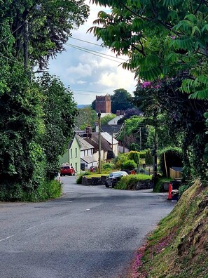 Una calle tranquila con casas, una torre y abundante vegetación.