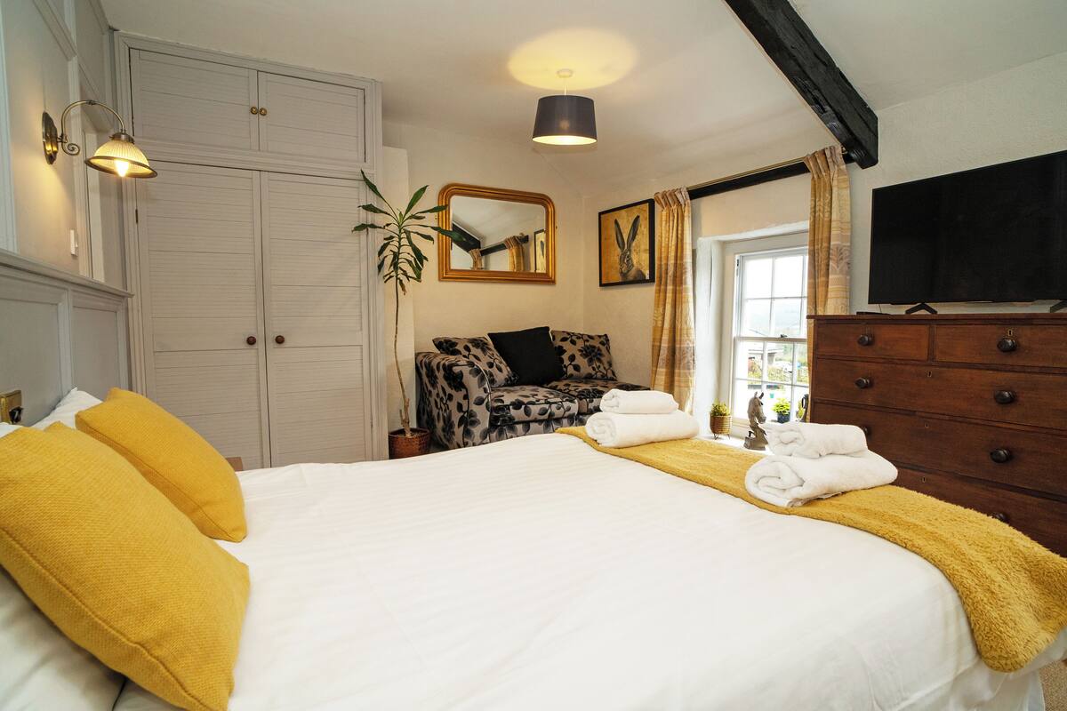 A hotel room with a large bed, a wardrobe, a dresser, a television, and a window with curtains.