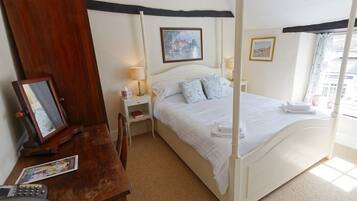 A four-poster bed with white bedding, a wooden desk with a telephone, and two framed pictures on the wall.