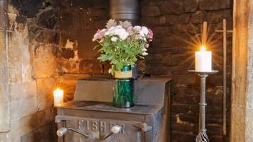 A vintage Fisher stove with a vase of flowers and candles, set against a stone wall.