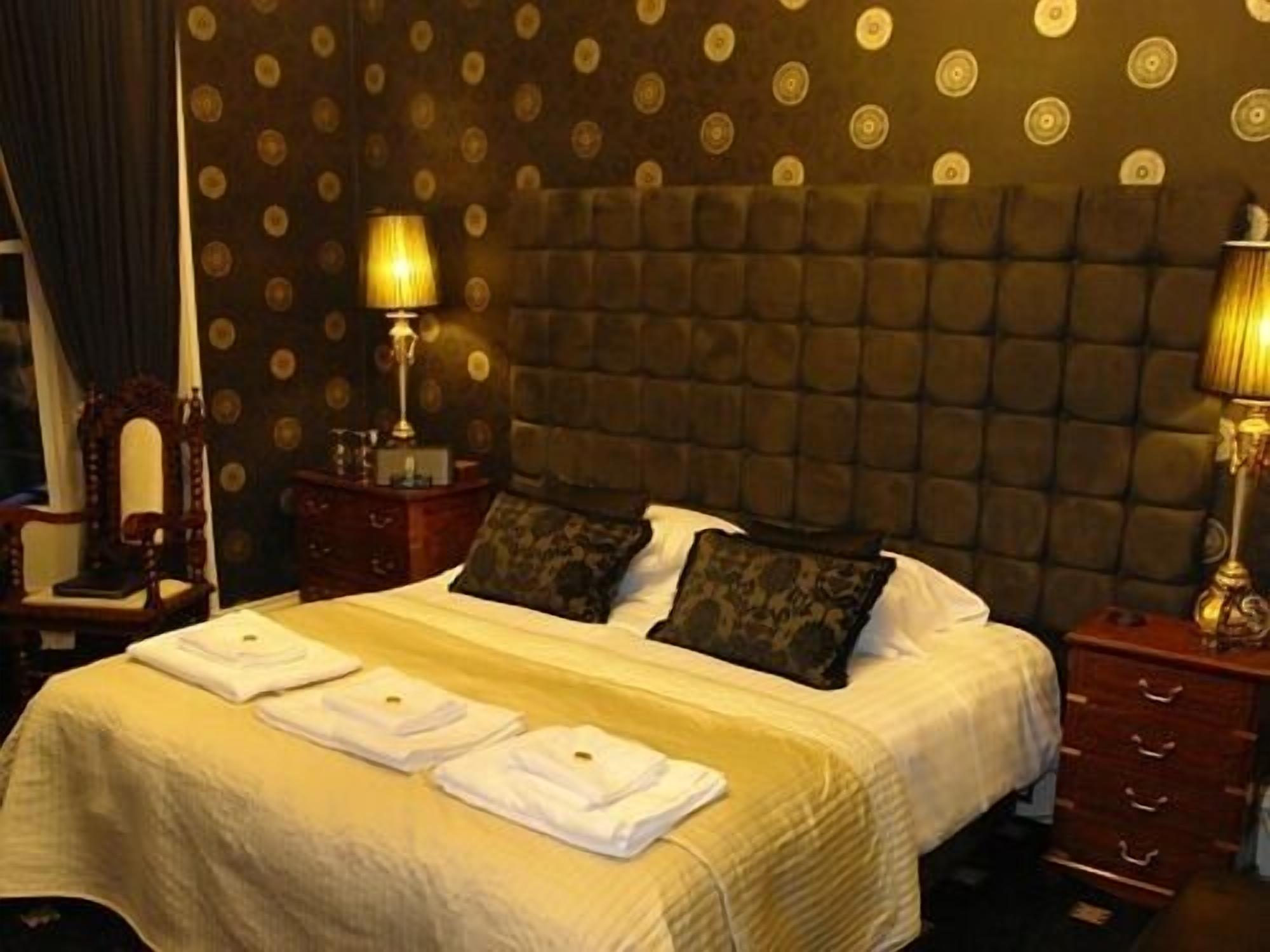 Una habitación de hotel con una cama grande, dos mesitas de noche, un cabecero y un papel tapiz estampado.