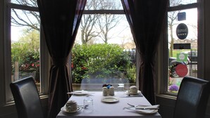 Une table à manger dressée pour deux personnes, avec vue sur un jardin par la fenêtre.