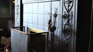 Une cheminée ornée de motifs métalliques complexes et un vase contenant des plantes séchées.