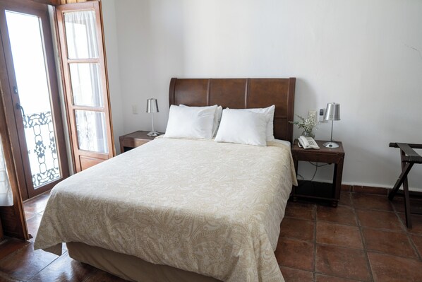 A neatly made bed with a patterned bedspread, a wooden headboard, and two bedside tables with lamps and a phone. - Casa Aspeytia Hotel Boutique (Querétaro)