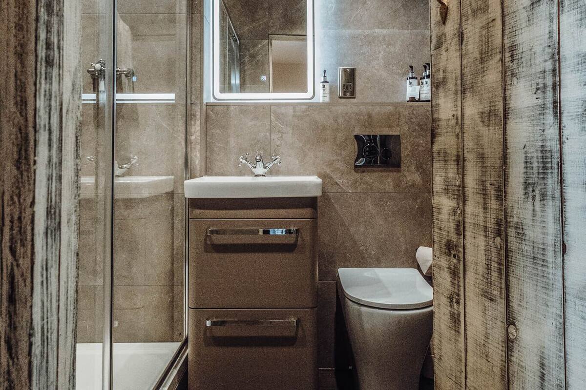 A narrow bathroom with a glass shower enclosure, a wooden vanity, and a toilet.
