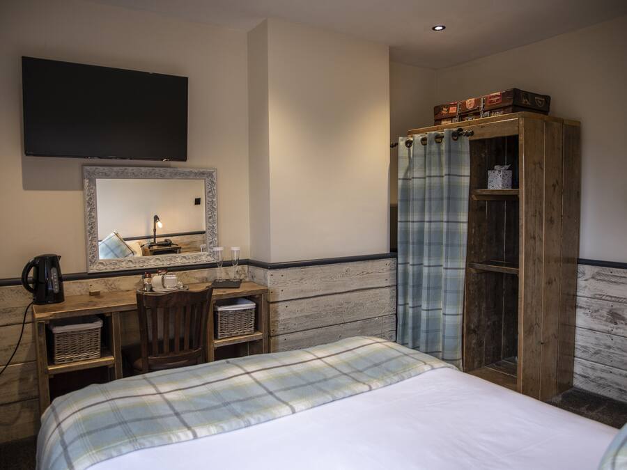 Quarto de hotel com cama, secretária com espelho, televisão, guarda-roupa e zona de duche.