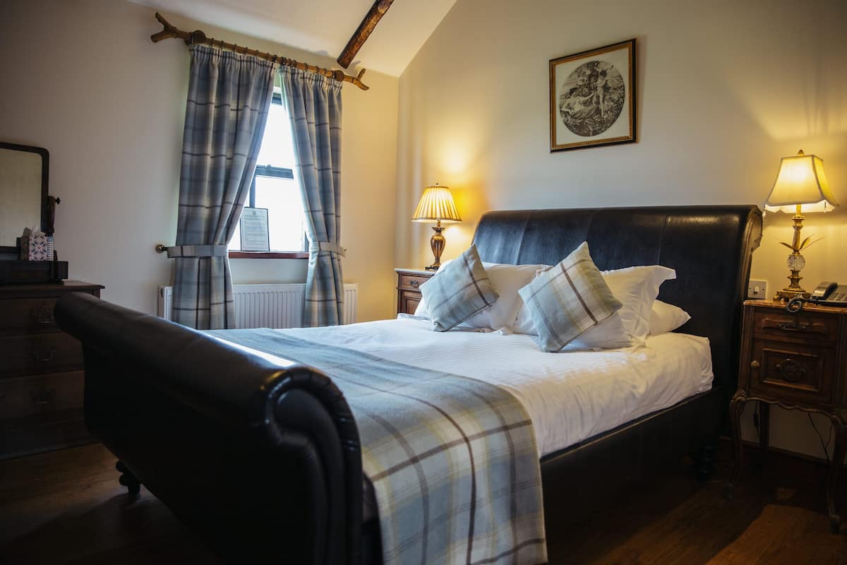 A bedroom with a bed, two bedside tables with lamps, a window with curtains, a wooden chair, and a framed picture on the wall.