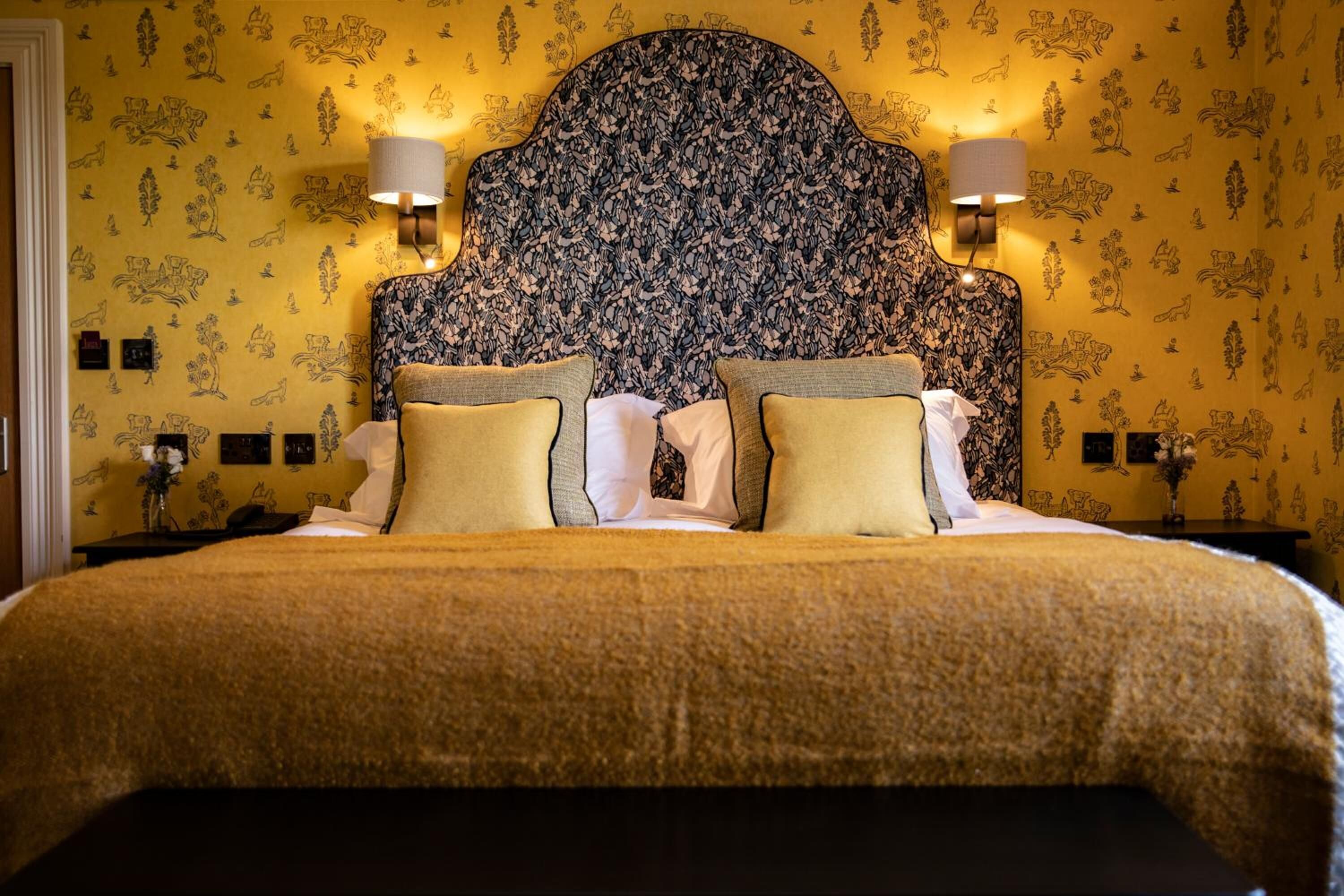 A double bed with a floral headboard, two bedside lamps, and a patterned wall.