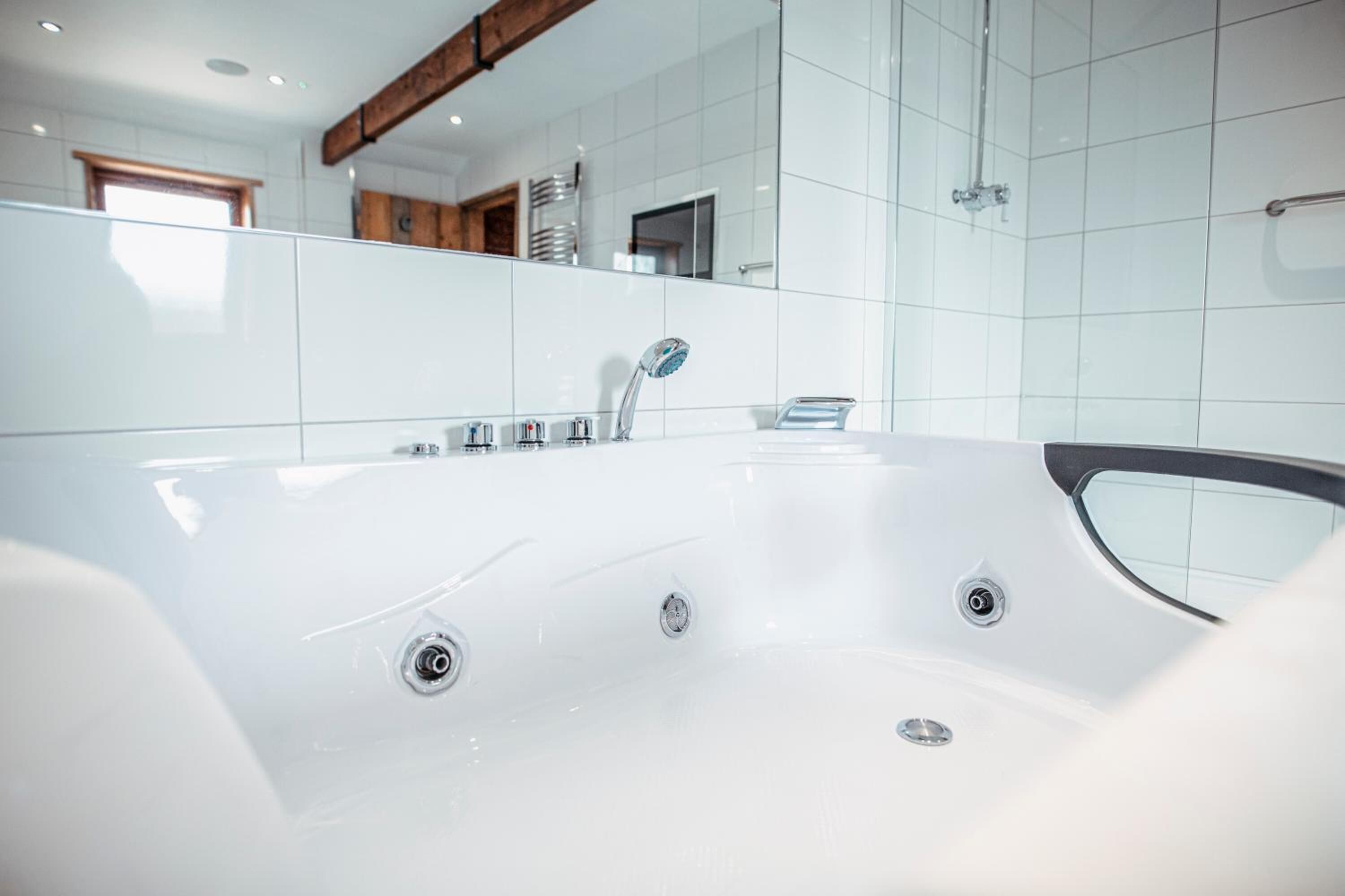 Een moderne badkamer met een ruime badkuip, witte tegels en een houten balk.