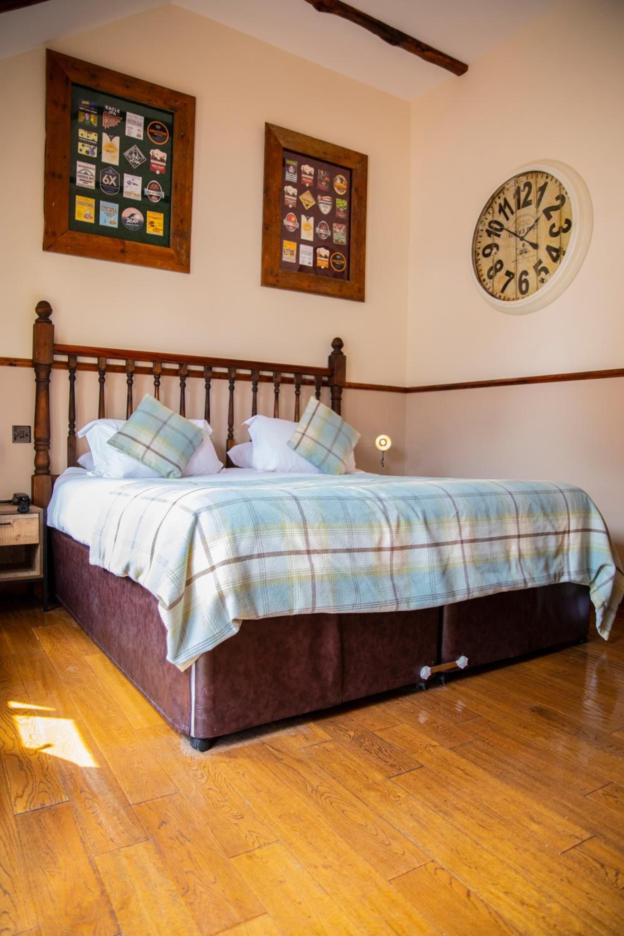 Ein Schlafzimmer mit einem hölzernen Bett, einer karierten Tagesdecke und zwei gerahmten Sammlungen an der Wand.
