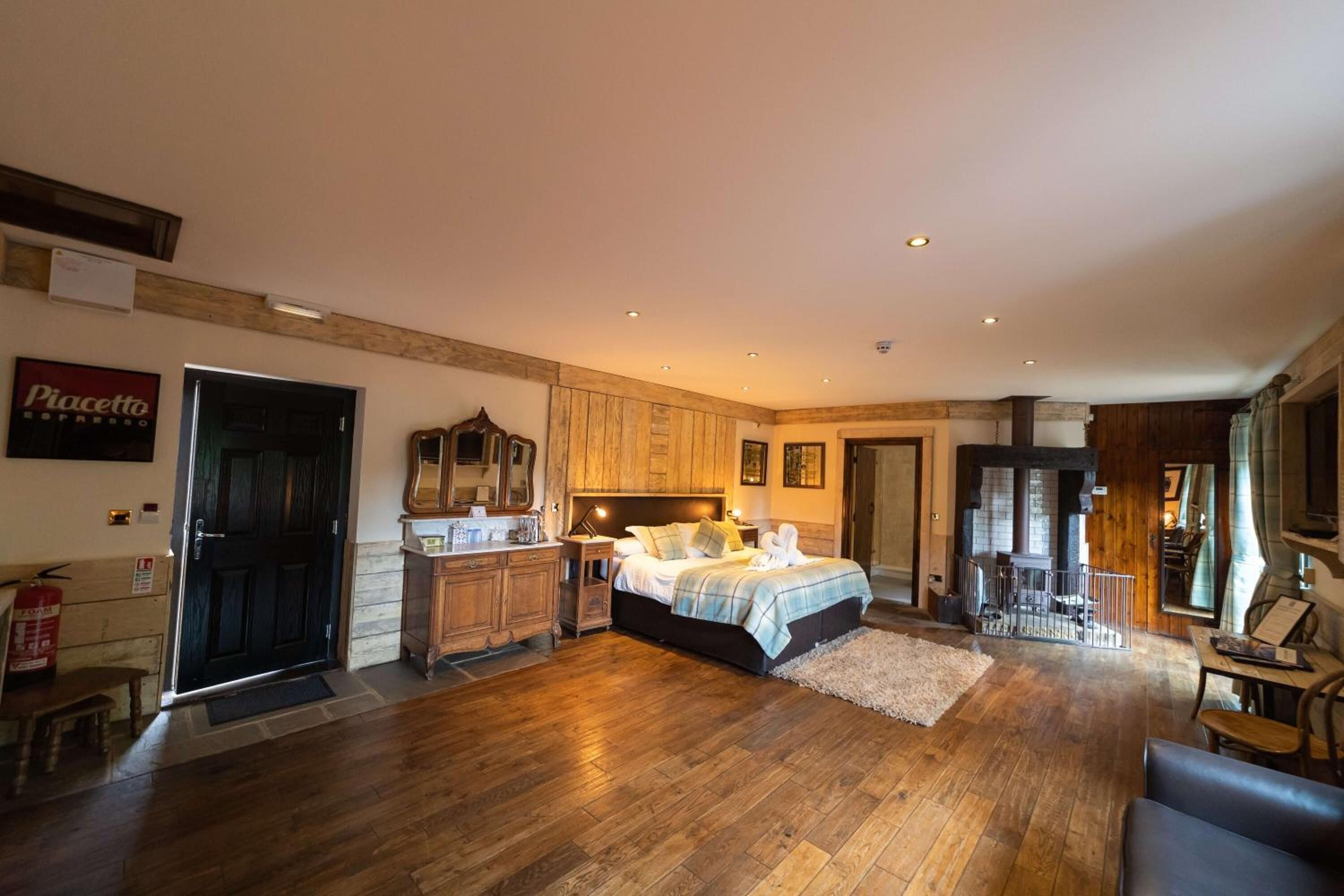 A spacious bedroom with a large bed, wooden flooring, a sitting area with a table and chairs, and a view of the outside through a window.