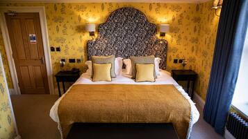 Habitación de hotel con una cama grande, dos mesitas de noche, un banco, papel tapiz floral y una puerta de madera.