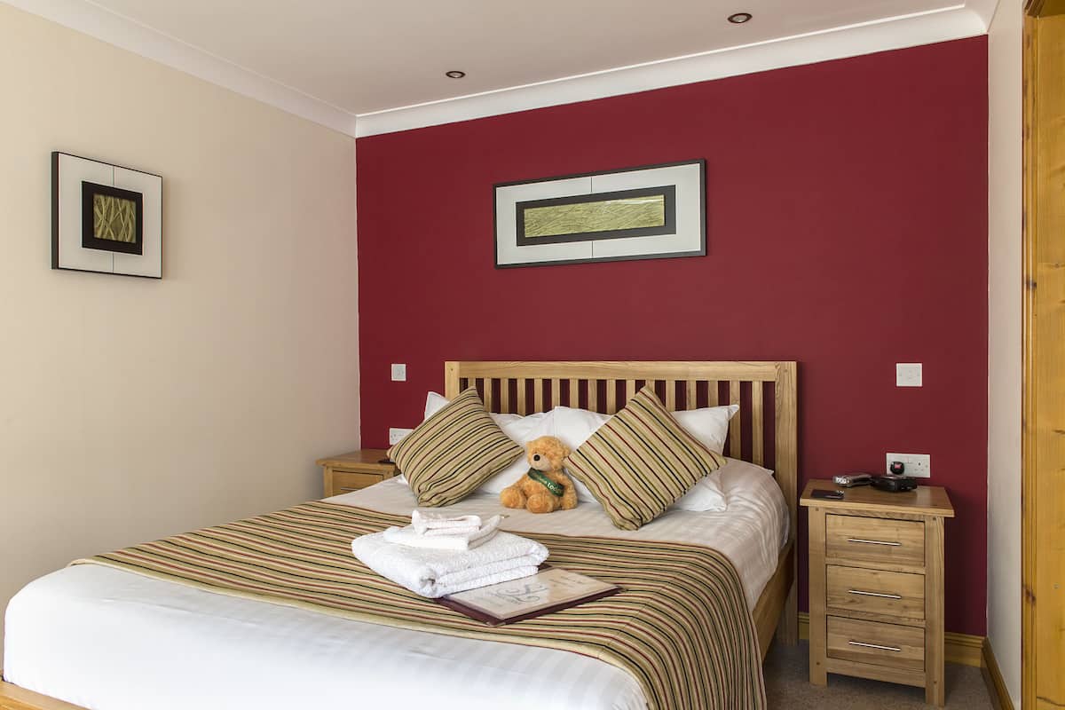 A neatly made bed with striped bedding, a teddy bear, and pillows on a wooden headboard.