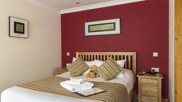 A neatly made bed with striped bedding, a teddy bear, and pillows on a wooden headboard.