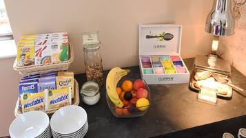Mesa de buffet de café da manhã com cereais, Weetabix, frutas e uma caixa de chá Clipper.