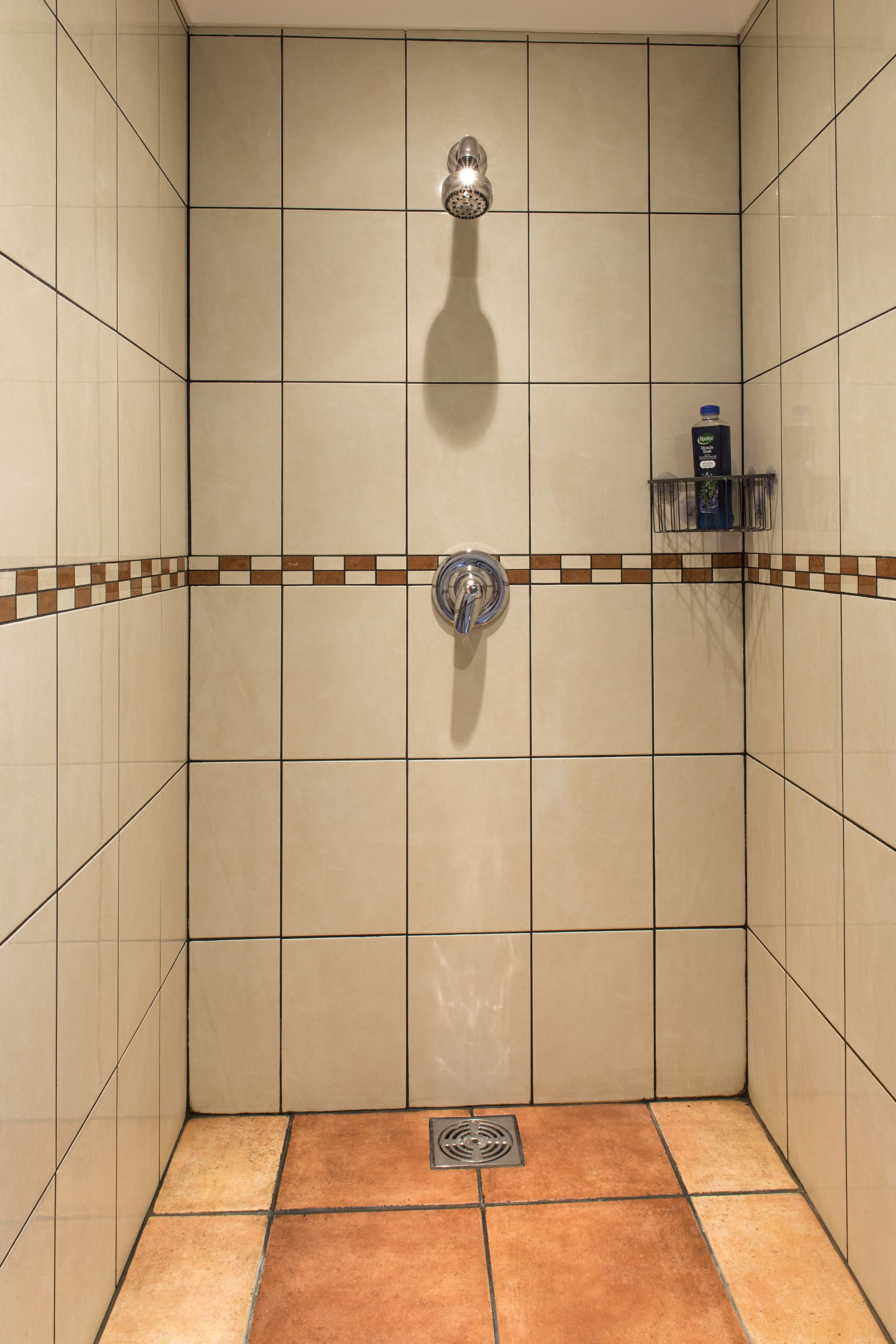 A small, tiled shower with a handheld showerhead and a soap dispenser on a shelf.