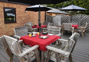 An outdoor dining area with wooden tables and chairs, covered by red tablecloths and black umbrellas. - Spanhoe Lodge - B&B (Corby)