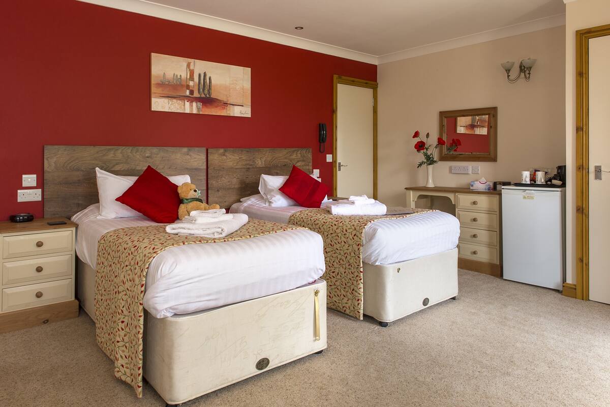 A hotel room with two beds, a desk, a mirror, and a small kitchenette.