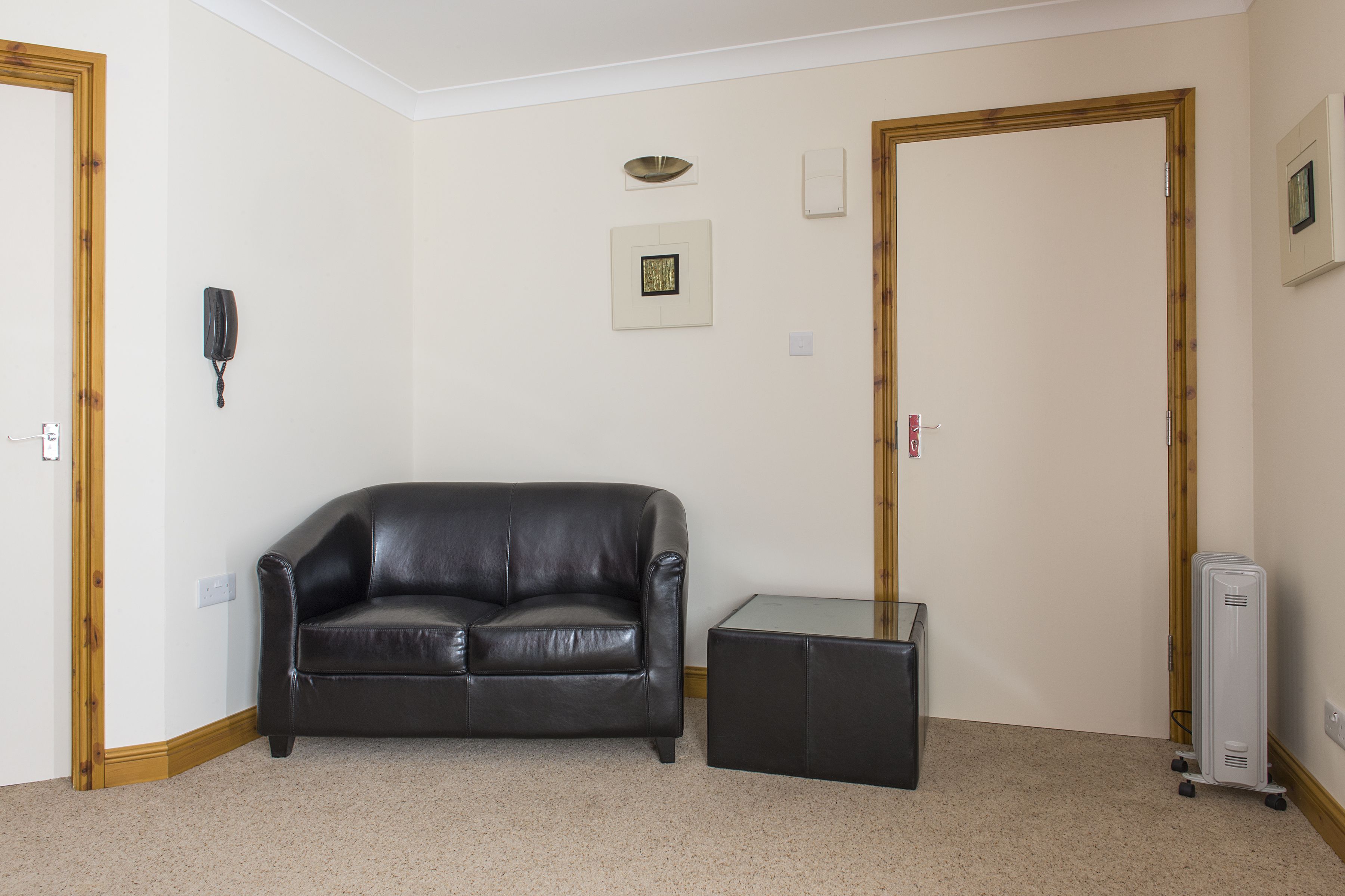 Una habitación con un sofá de cuero negro, una mesa de centro de vidrio y un calentador portátil blanco.