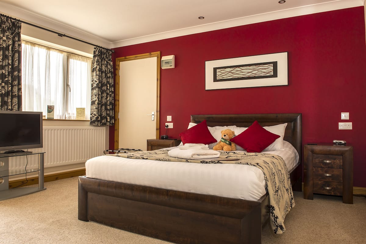 A bedroom with a large bed, a bedside table, a TV, and a window with curtains.