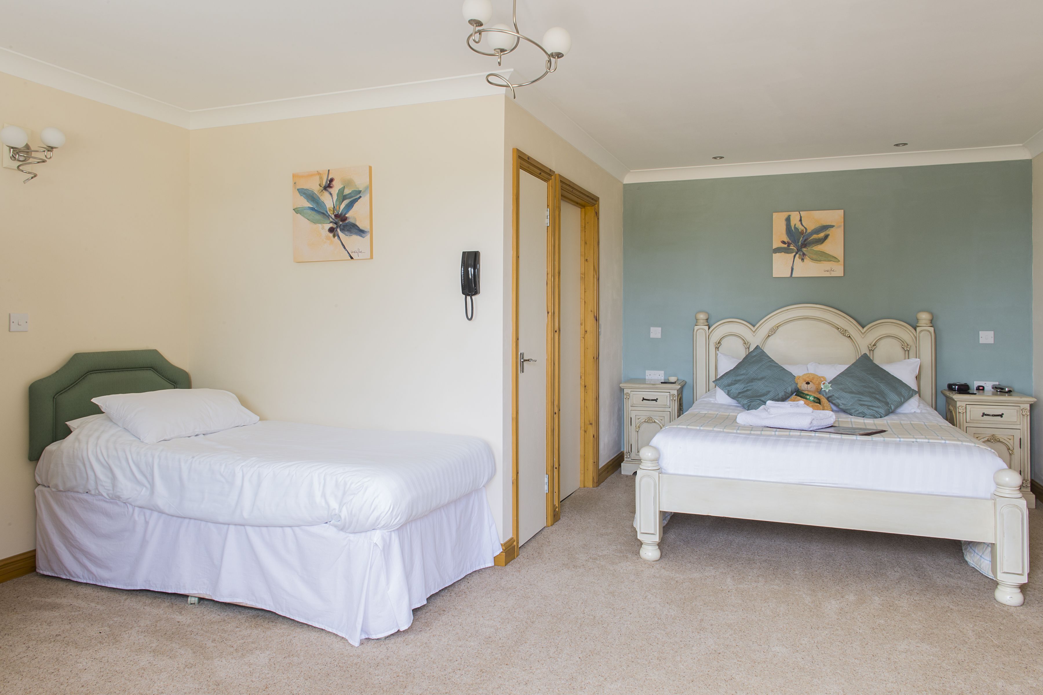 A bedroom with two beds, a wooden door, a nightstand, and a wall-mounted telephone.