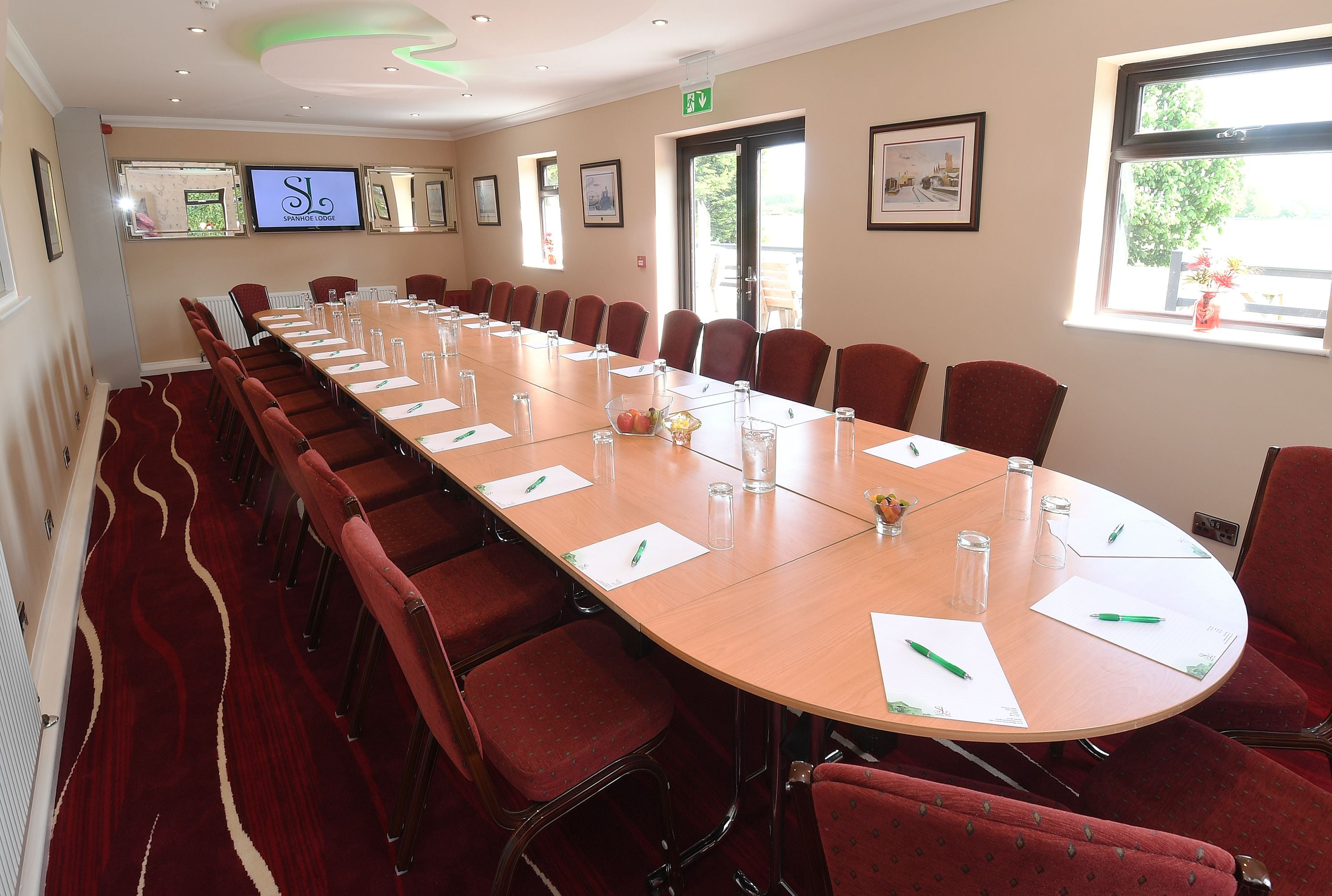 A conference room with a long table, red chairs, and a television screen on the wall.
