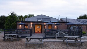 A building with a brick facade, a wooden deck, and outdoor seating with umbrellas. - Spanhoe Lodge - B&B (Corby)