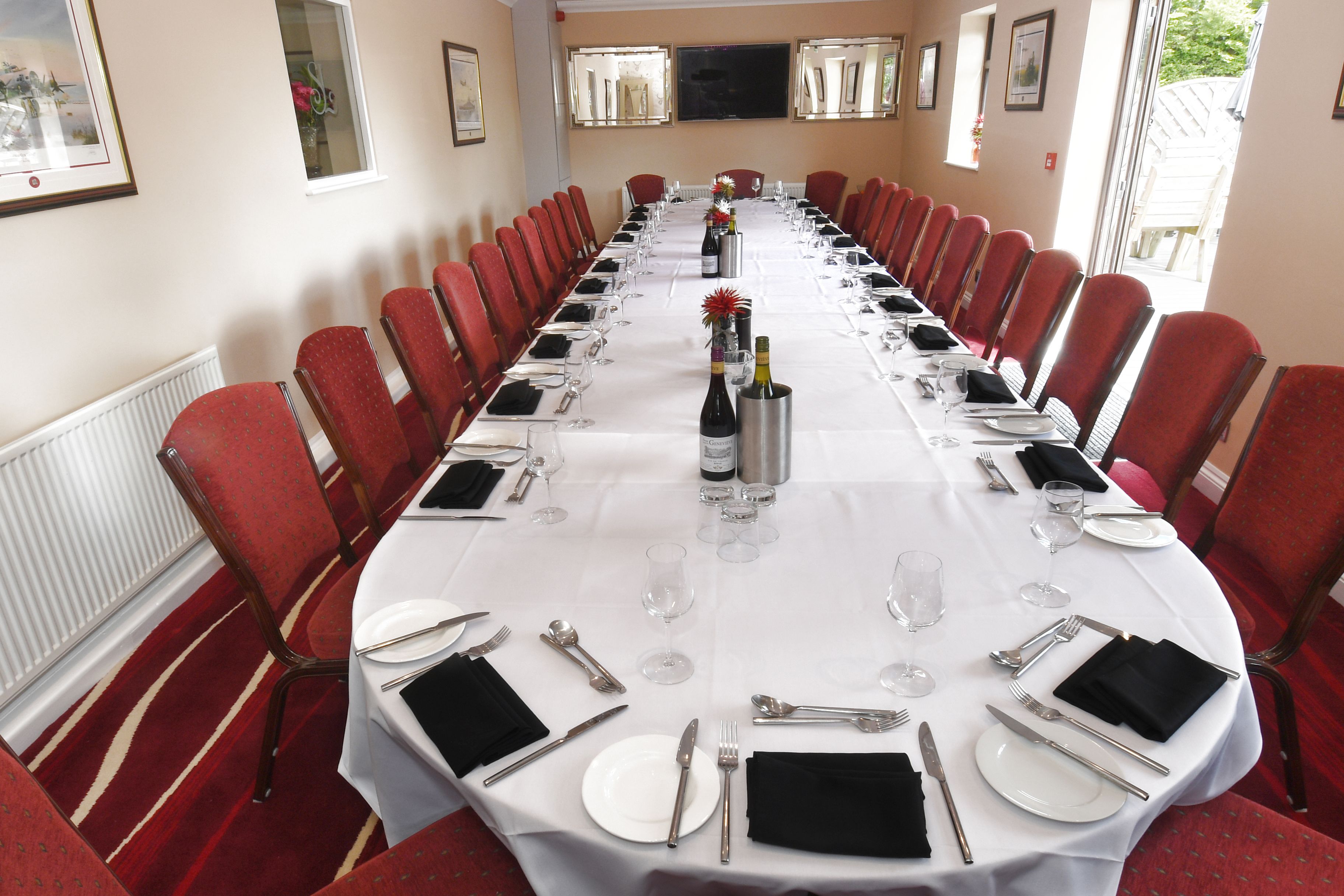 A conference room with a long table set for a formal event, surrounded by red chairs.