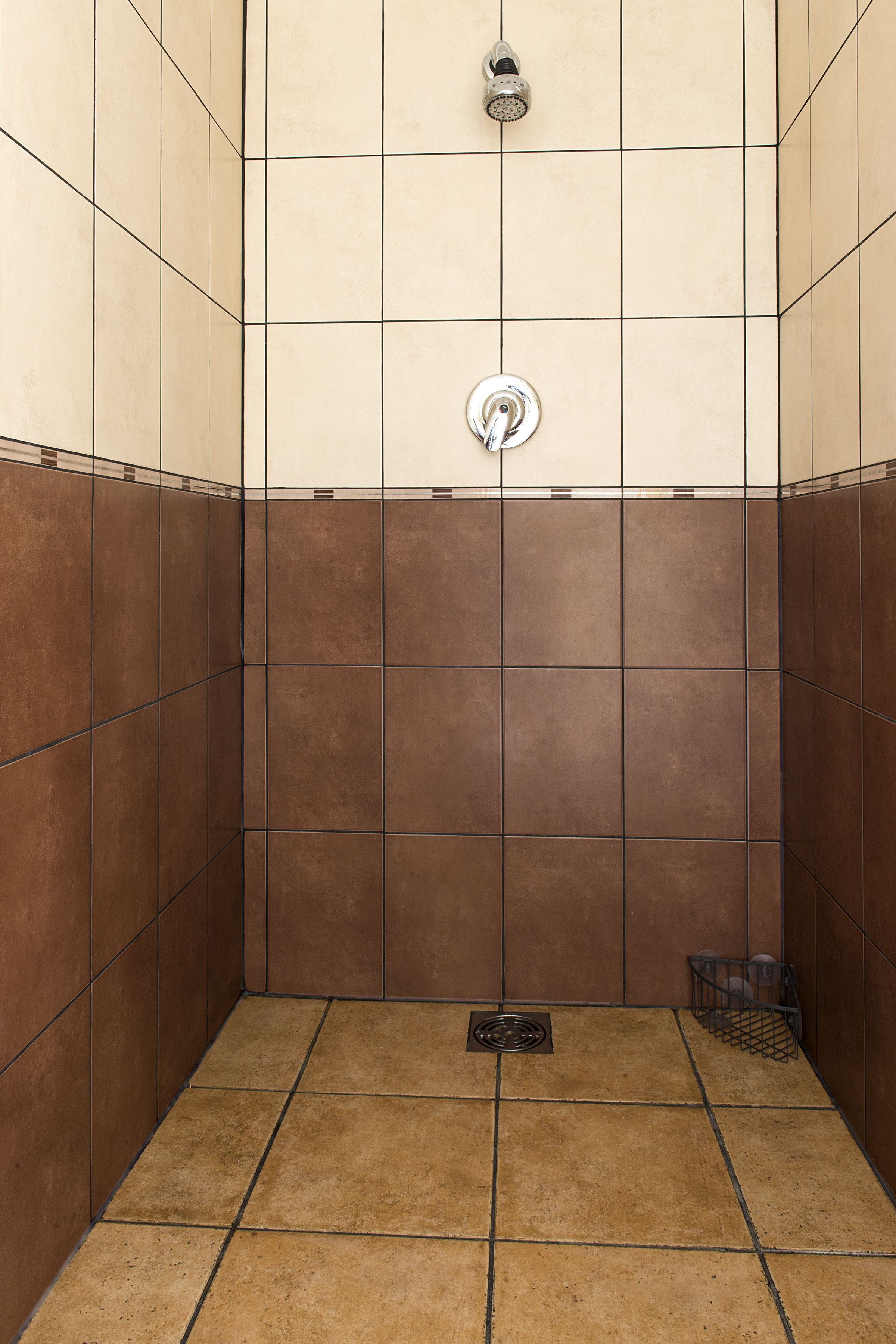 Área de chuveiro com azulejos, um ralo e uma estante de metal.