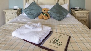 A neatly made bed with a plush teddy bear, two pillows, a folded towel, and a guest directory book. - Spanhoe Lodge - B&B (Corby)