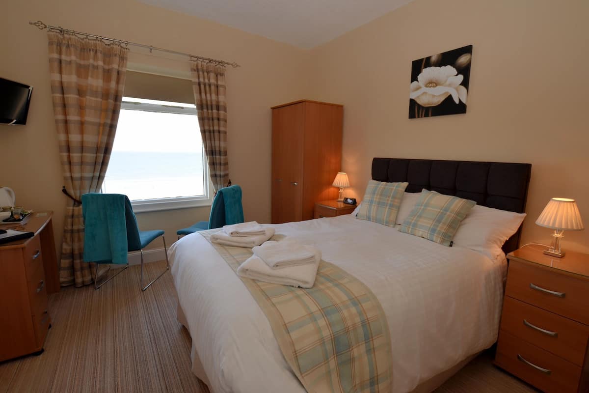 A neatly made bed with a plaid bedspread, a bedside lamp, and a window with curtains.