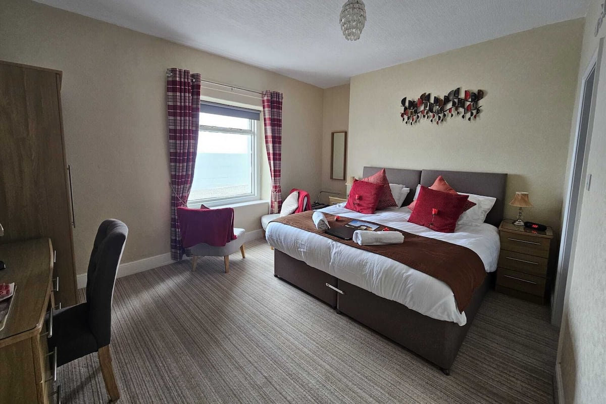 A bedroom with a bed, bedside table, lamp, and a window with curtains.