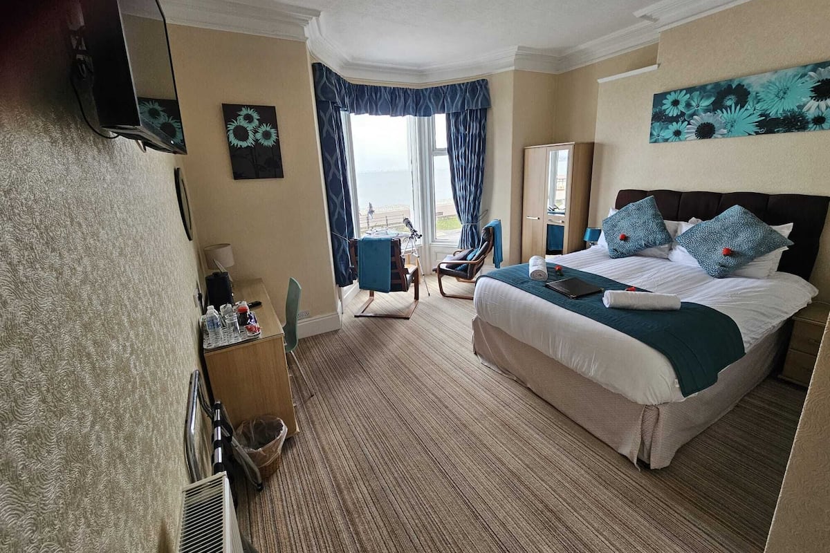 A hotel room with a large bed, a desk, a chair, and a view of the sea.