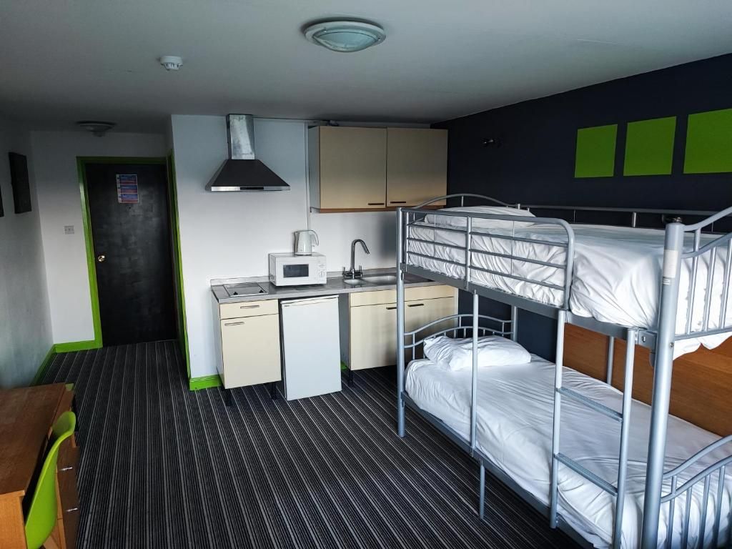 A compact room with bunk beds, a kitchenette, and a small desk area.