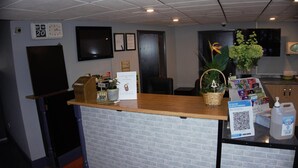A reception area with a wooden counter, a clock, a television, and a plant. - Happy Guests Lodge (Warrington)