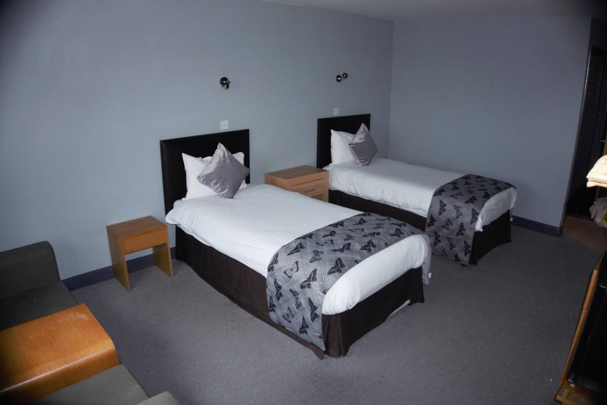 A room with two single beds, each with a headboard, a bedside table, and a small wooden stool.