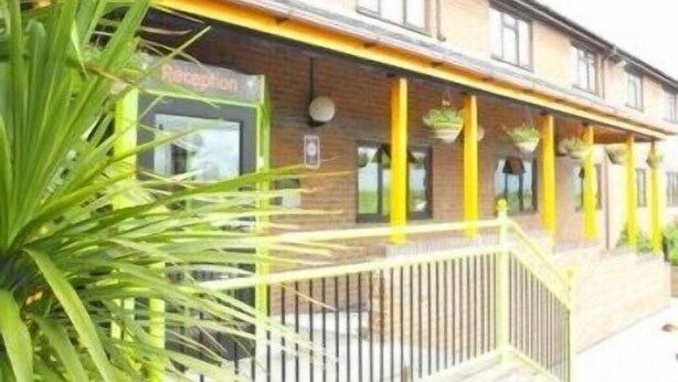 A building with a reception area, yellow pillars, and a staircase leading to the entrance. - Happy Guests Lodge (Warrington)