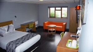 A hotel room with a bed, a desk with a telephone and a hairdryer, an orange sofa, and a window with a view of greenery. - Happy Guests Lodge (Warrington)