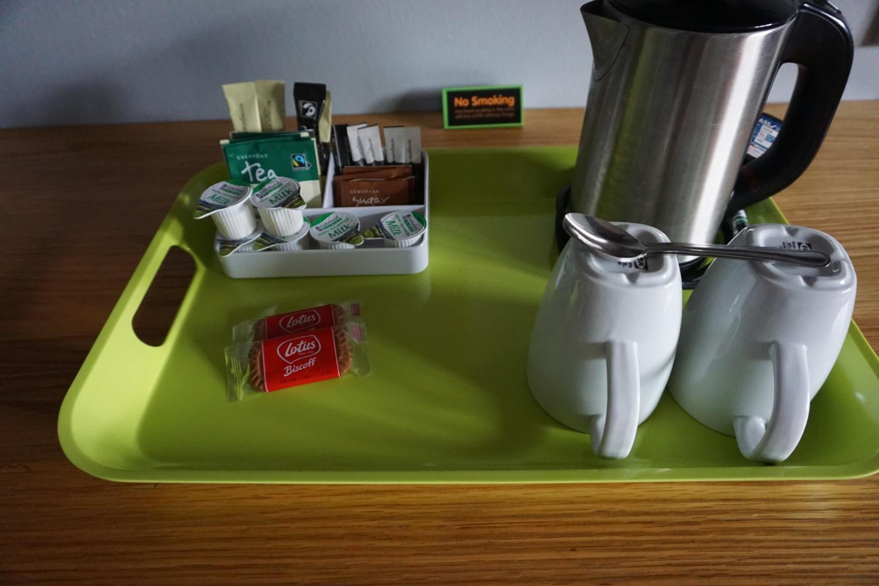 A tray with a teapot, teacups, a box of tea, and a packet of biscuits.