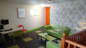 A room with a green sofa, a desk with a computer, a red chair, and a patterned wallpaper. - Happy Guests Lodge (Warrington)
