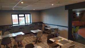 A conference room with multiple tables and chairs, a large window with a view of the outside, and a separate area with orange seating. - Happy Guests Lodge (Warrington)