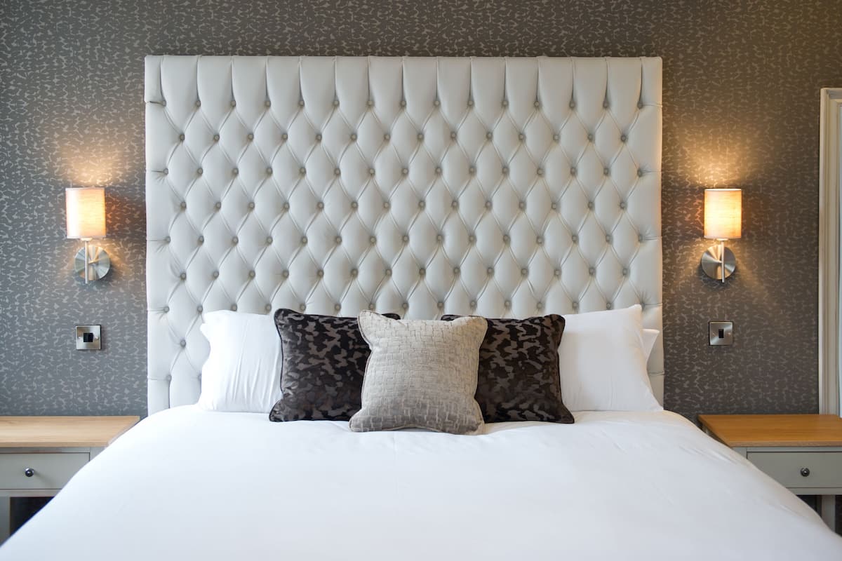 Una cama bien tendida con cabecera capitonada, dos lámparas de noche y almohadas estampadas.