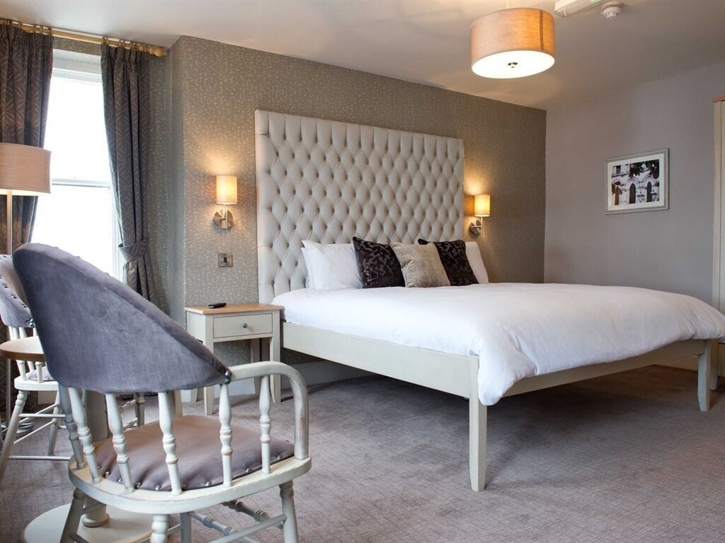 A bedroom with a large bed, a tufted headboard, bedside lamps, a chair, and a small table.