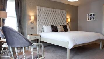 A bedroom with a large bed, a tufted headboard, bedside lamps, a chair, and a small table.