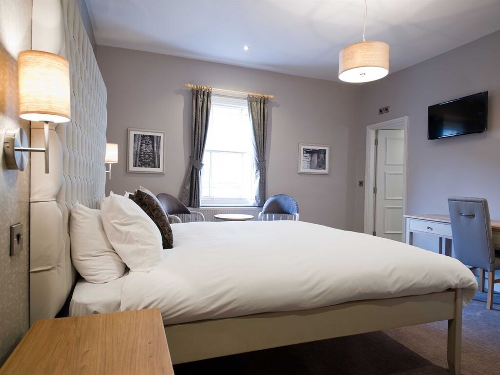 A hotel room with a large bed, bedside lamps, a desk, and a TV on the wall.