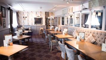 Un restaurante con zona de bar, disposición de mesas y alfombra estampada.
